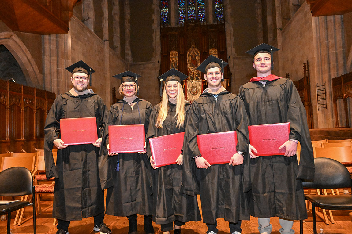 Graduates wearing caps and gowns hold their diplomas and smile